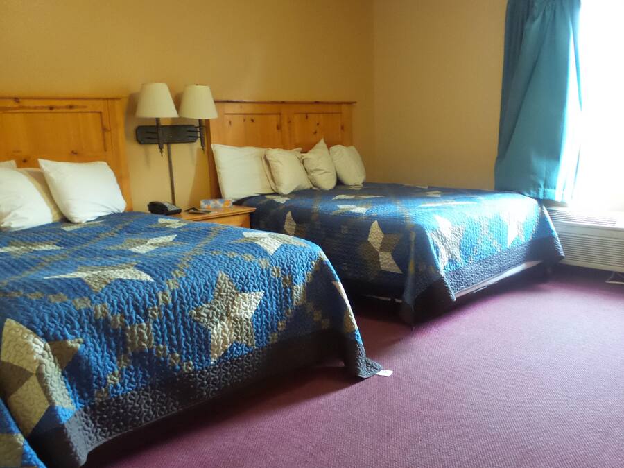 Two single beds with blue and beige patterned blankets, a wooden headboard, a nightstand with a lamp, and a window with a blue curtain.