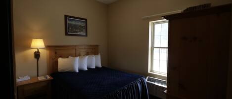 A bedroom with a bed, a nightstand, a lamp, a window, and a door.