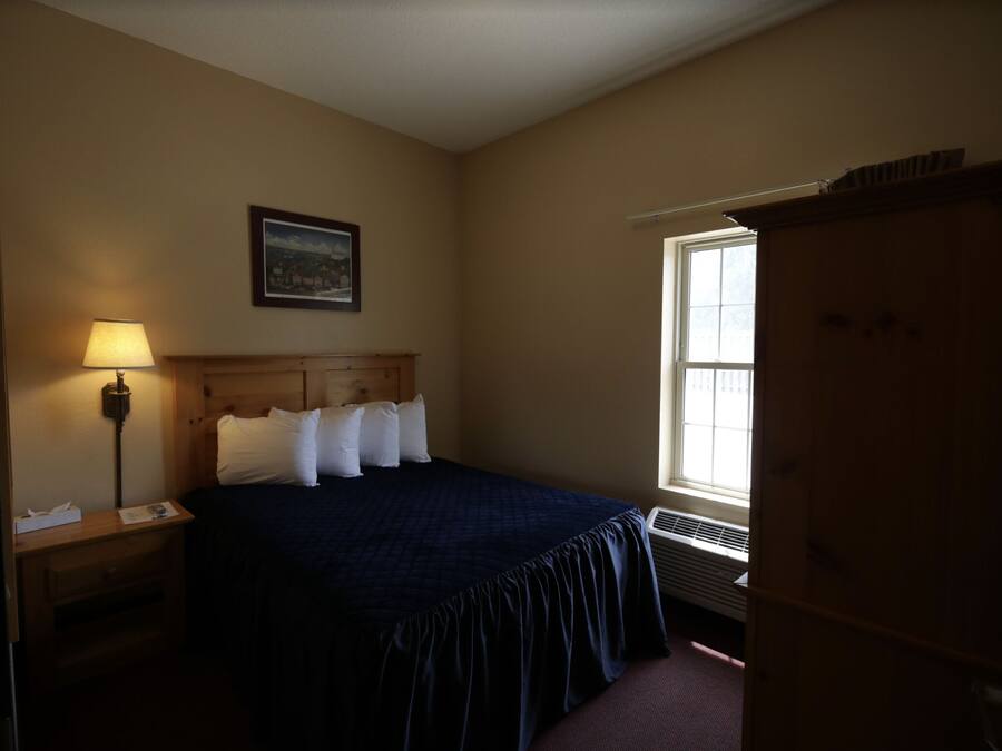 A bedroom with a bed, a nightstand, a lamp, a window, and a door.