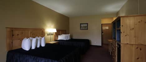 A hotel room with two beds, a wooden headboard, a desk with a lamp, a small cabinet, and a framed picture on the wall.