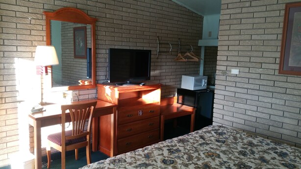 A room with a brick wall, a wooden desk with a television, a microwave, and a bed with a floral bedspread. - Budget Inn (Heber Springs)