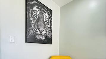 A room with a yellow armchair, a round wooden table with a vase of yellow flowers, and a black and white tiger painting on the wall.