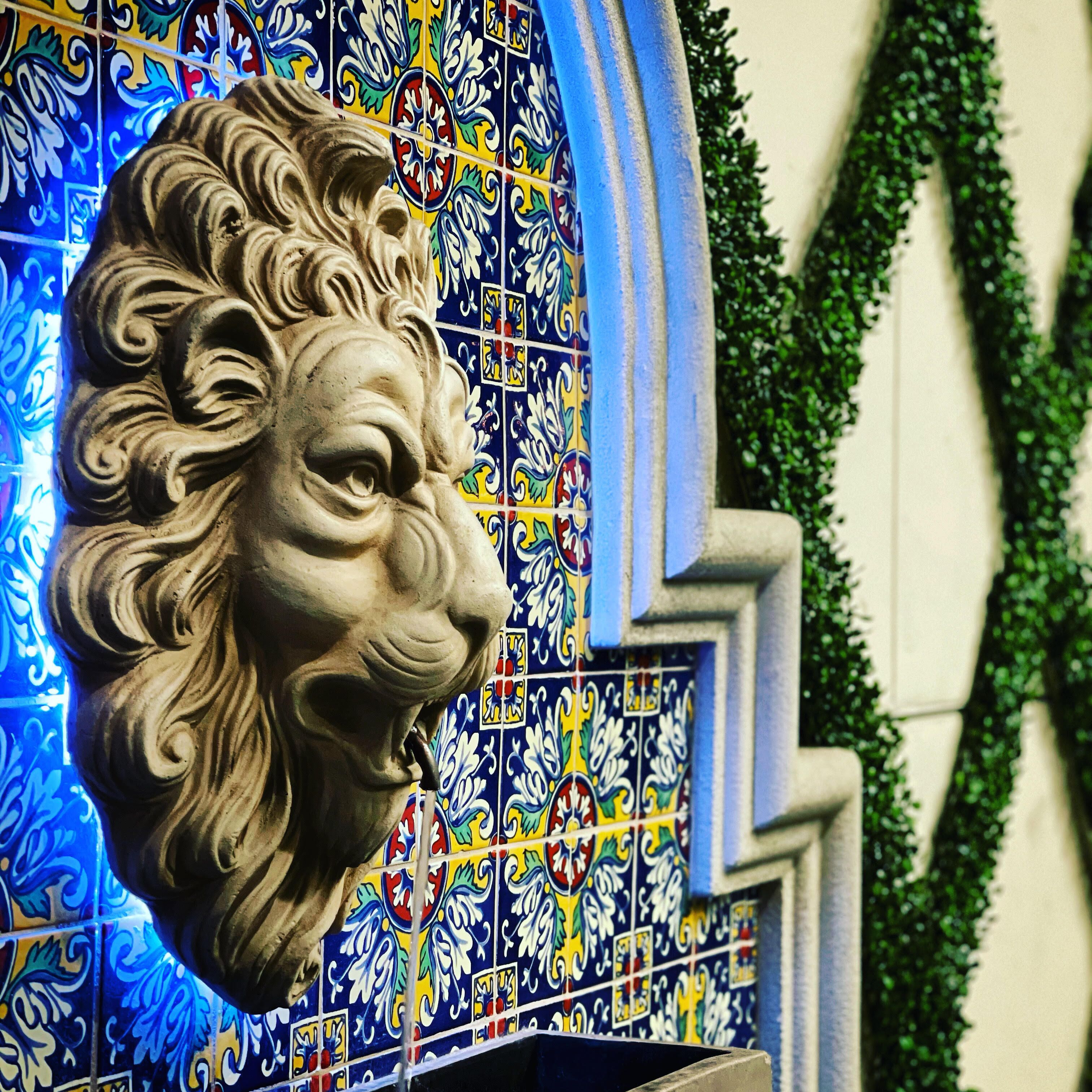 A stone lion head sculpture mounted on a wall with colorful tiles.