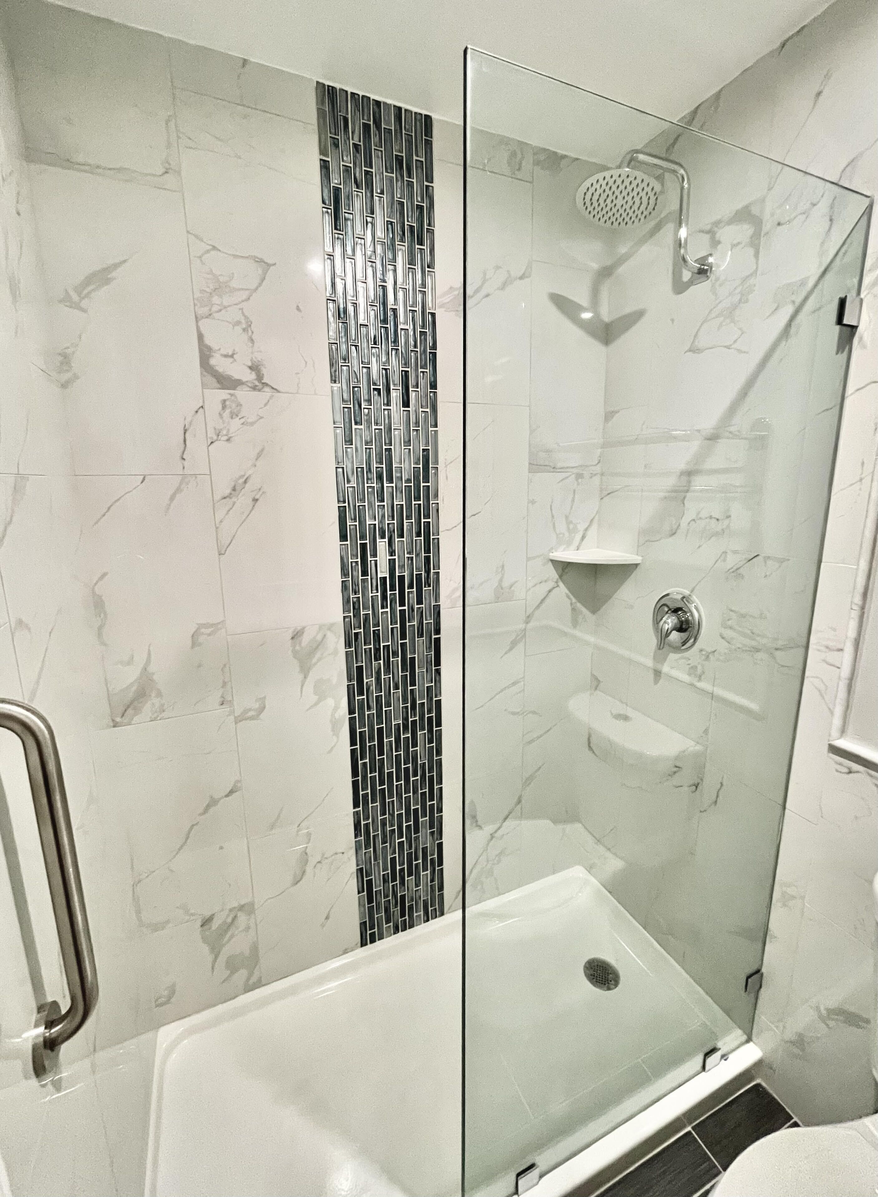 Un área de ducha moderna con puerta de vidrio, pared de azulejos con diseño vertical y una bañera blanca.