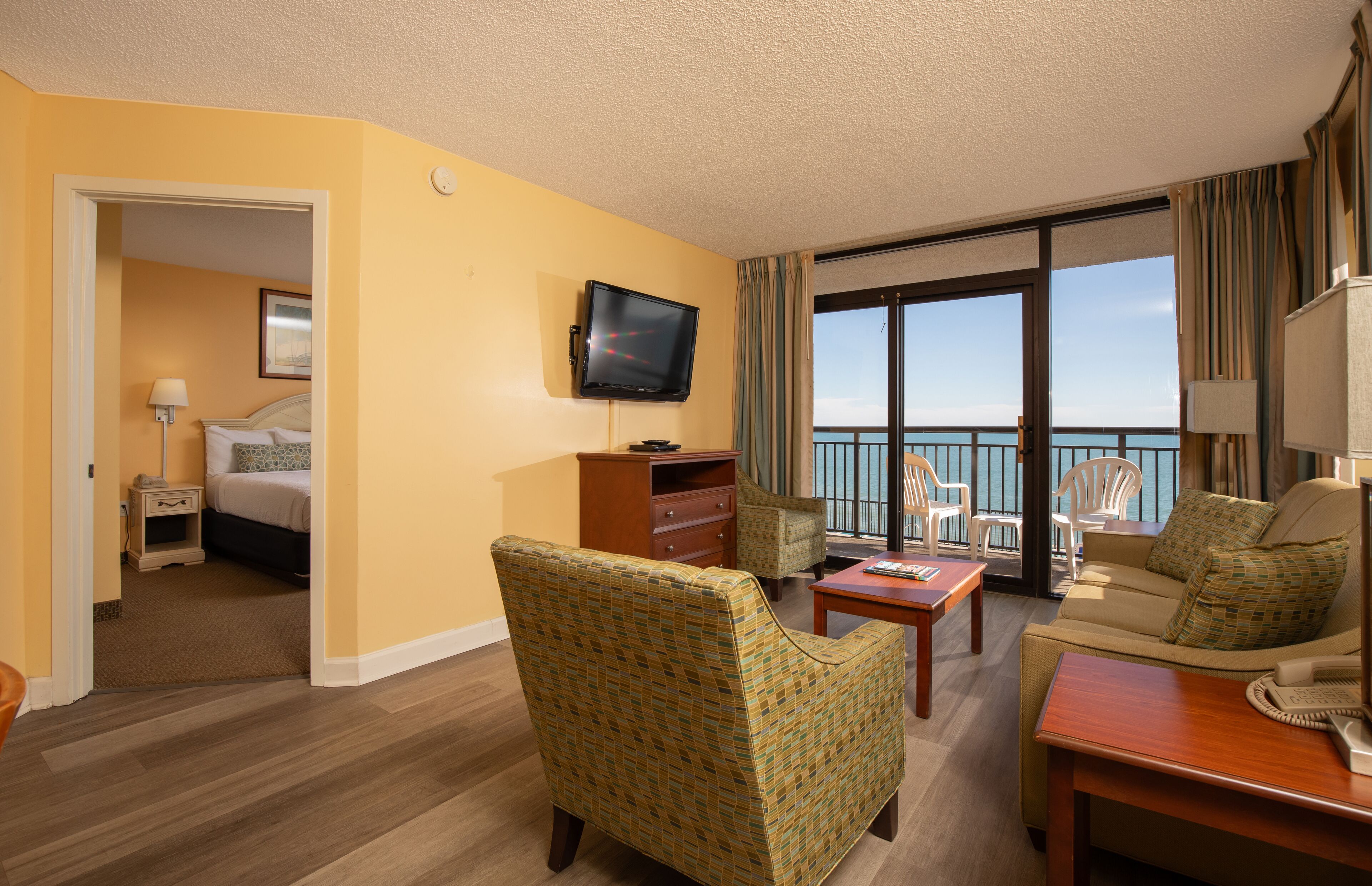 A hotel room with a balcony, a bed, a TV, a desk, and a chair.