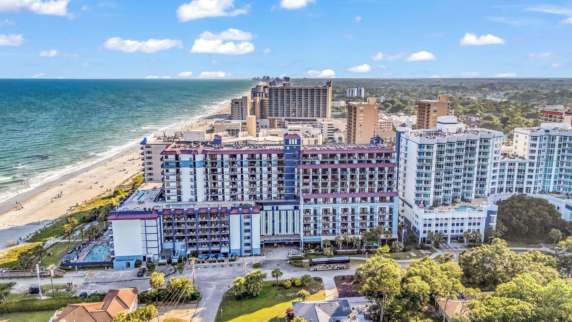A beachfront hotel with multiple buildings, a swimming pool, and a beach.