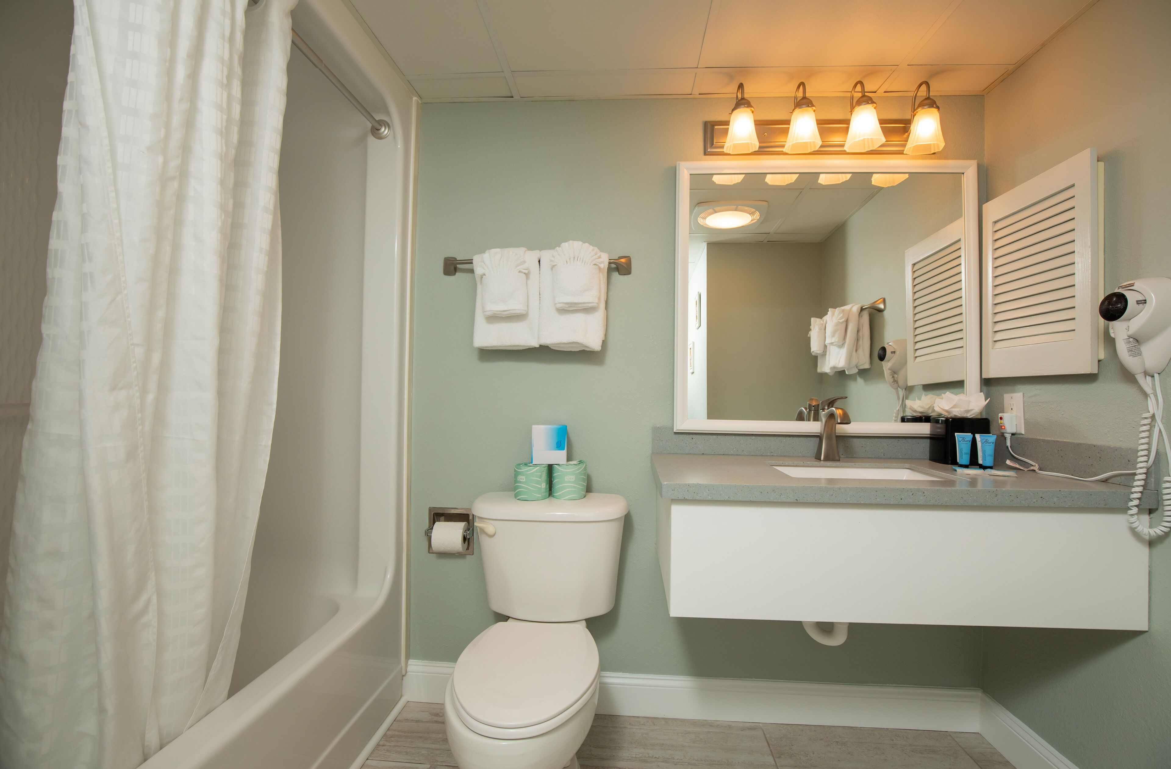 A bathroom with a toilet, sink, and mirror. There are towels hanging on a rack, a hairdryer, and toiletries on the sink.