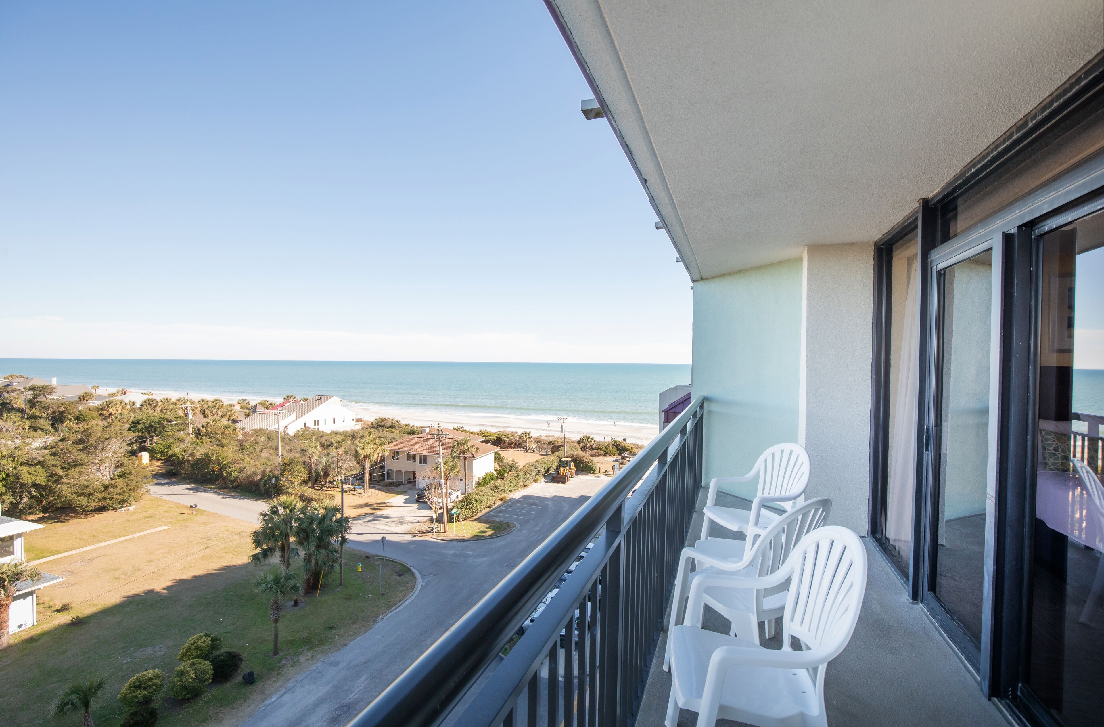 Uma varanda com cadeiras de plástico branco, com vista para a praia e área residencial.