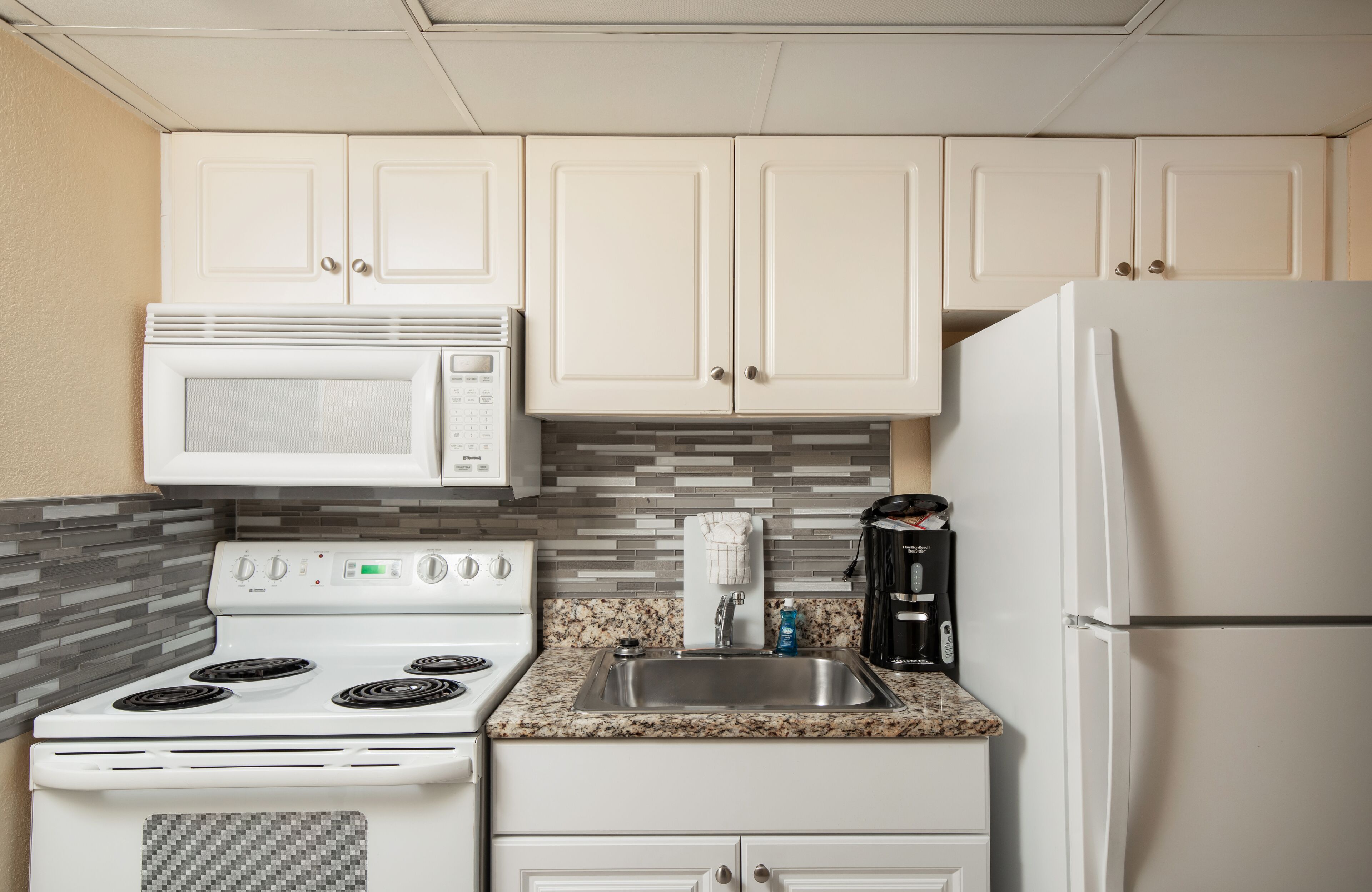 A kitchen with white cabinets, a white stove, a microwave, a sink, and a refrigerator.