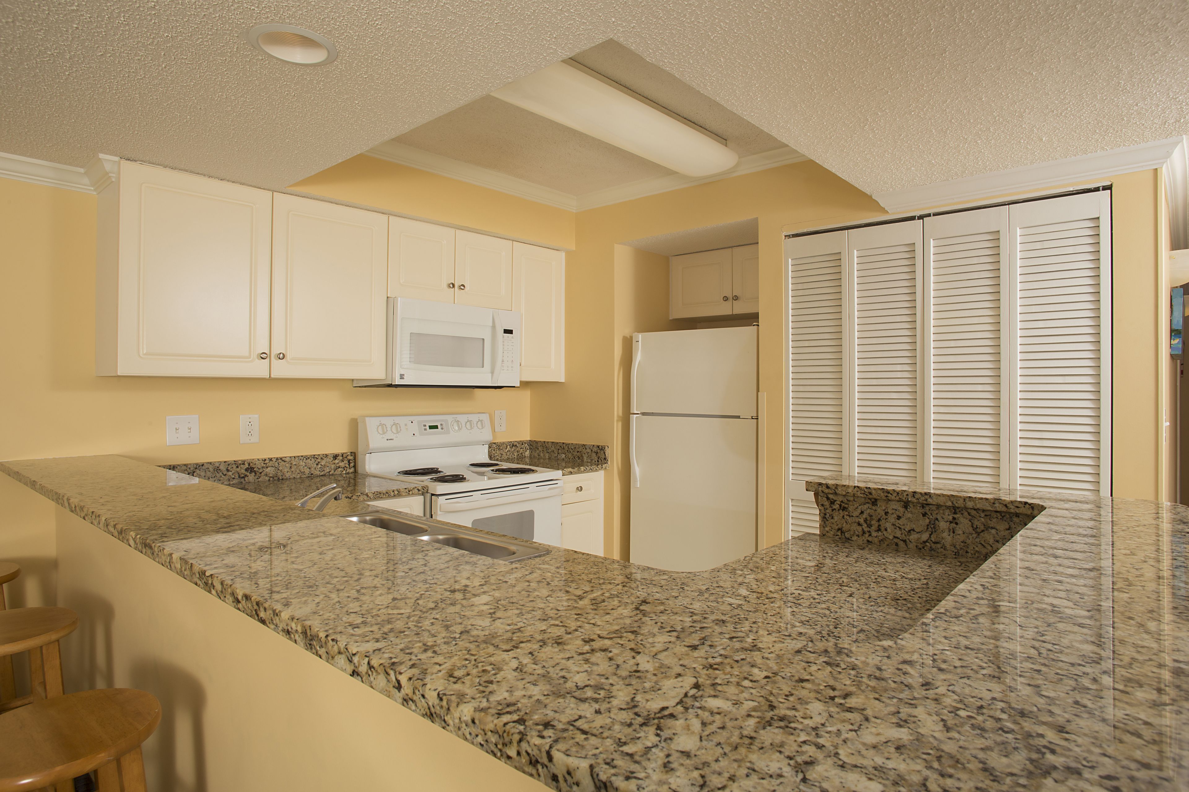 A kitchen with granite countertops, white cabinets, a microwave, a stove, and a refrigerator.