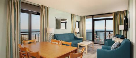 Habitación de hotel con una mesa de comedor, dos sofás y un balcón con vistas.