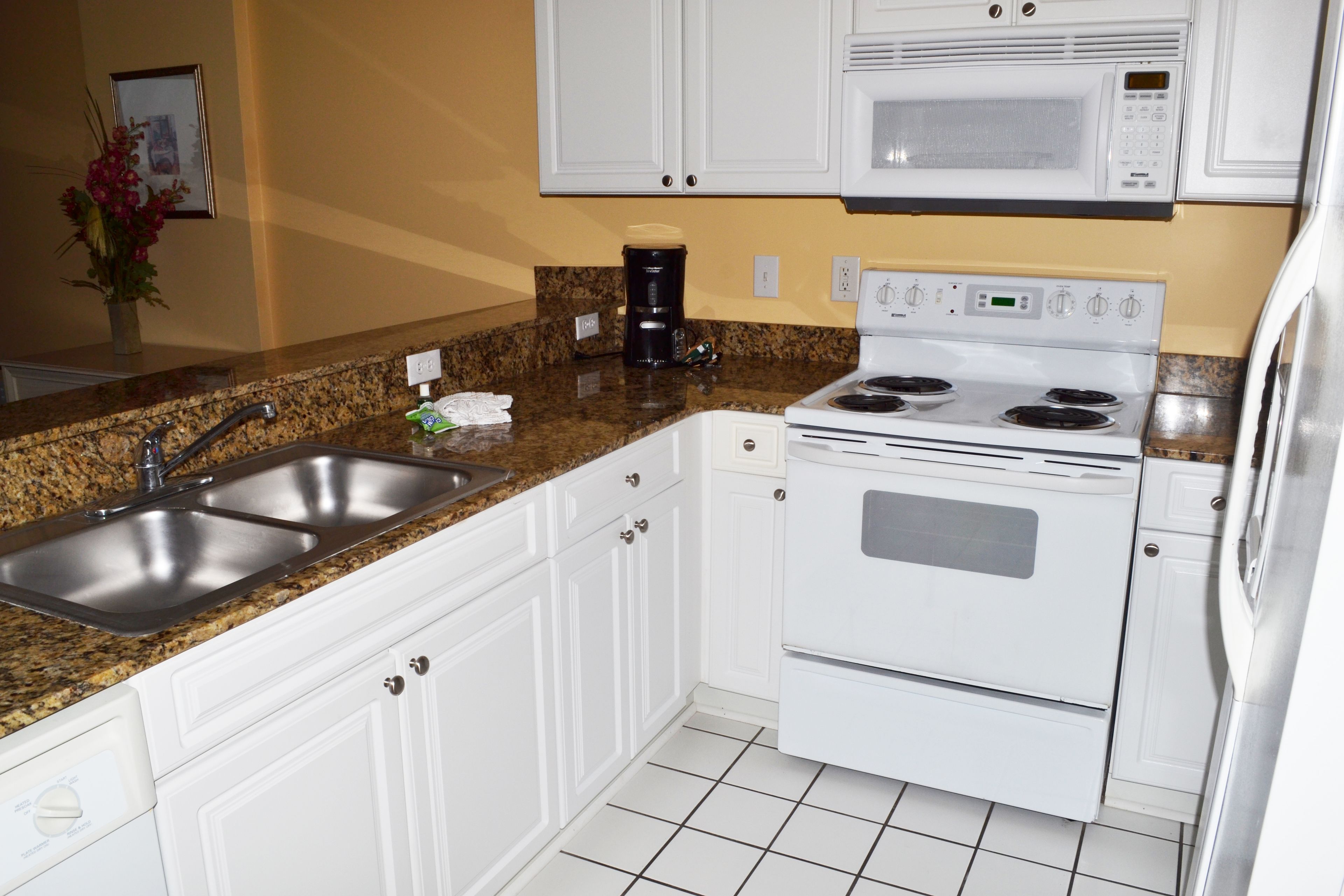 A kitchen with white cabinets, a double sink, a stove, and a microwave.