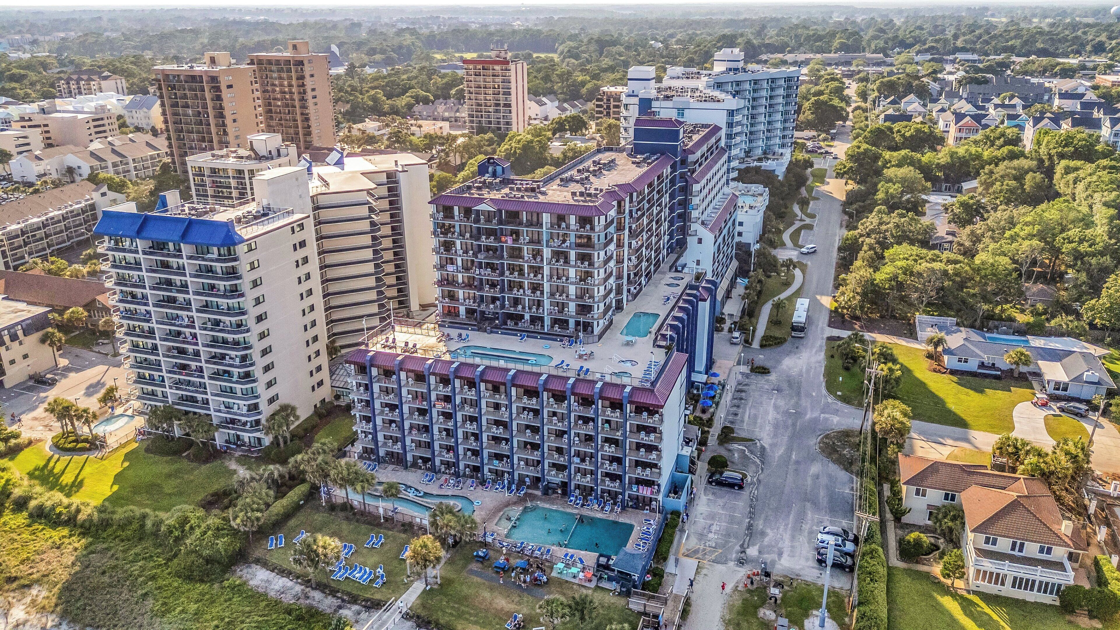 A high-rise hotel with multiple balconies, a swimming pool, and a parking area.