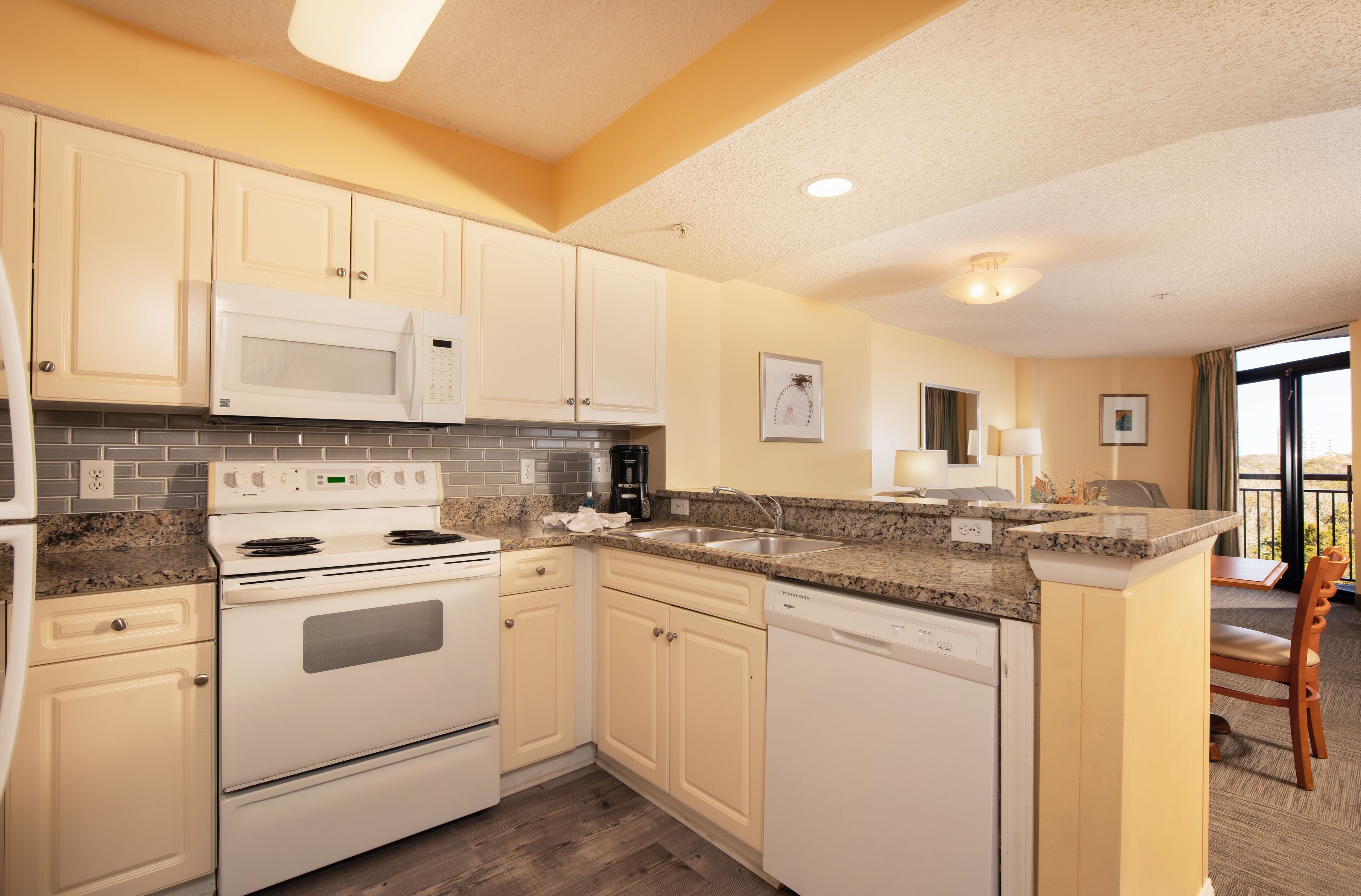 A kitchen with white cabinets, a microwave, stove, and dishwasher. There is a dining area with a table and chairs.