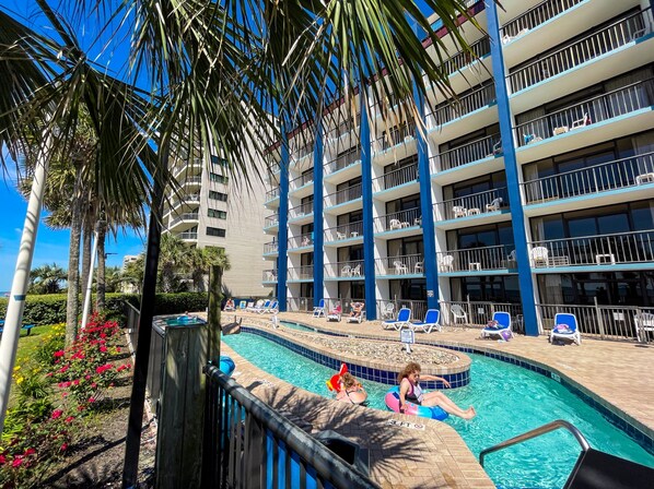 A hotel pool area with a clear view of the pool, lounge chairs, and a palm tree. - Grande Shores Ocean Resorts Condominiums (Myrtle Beach)