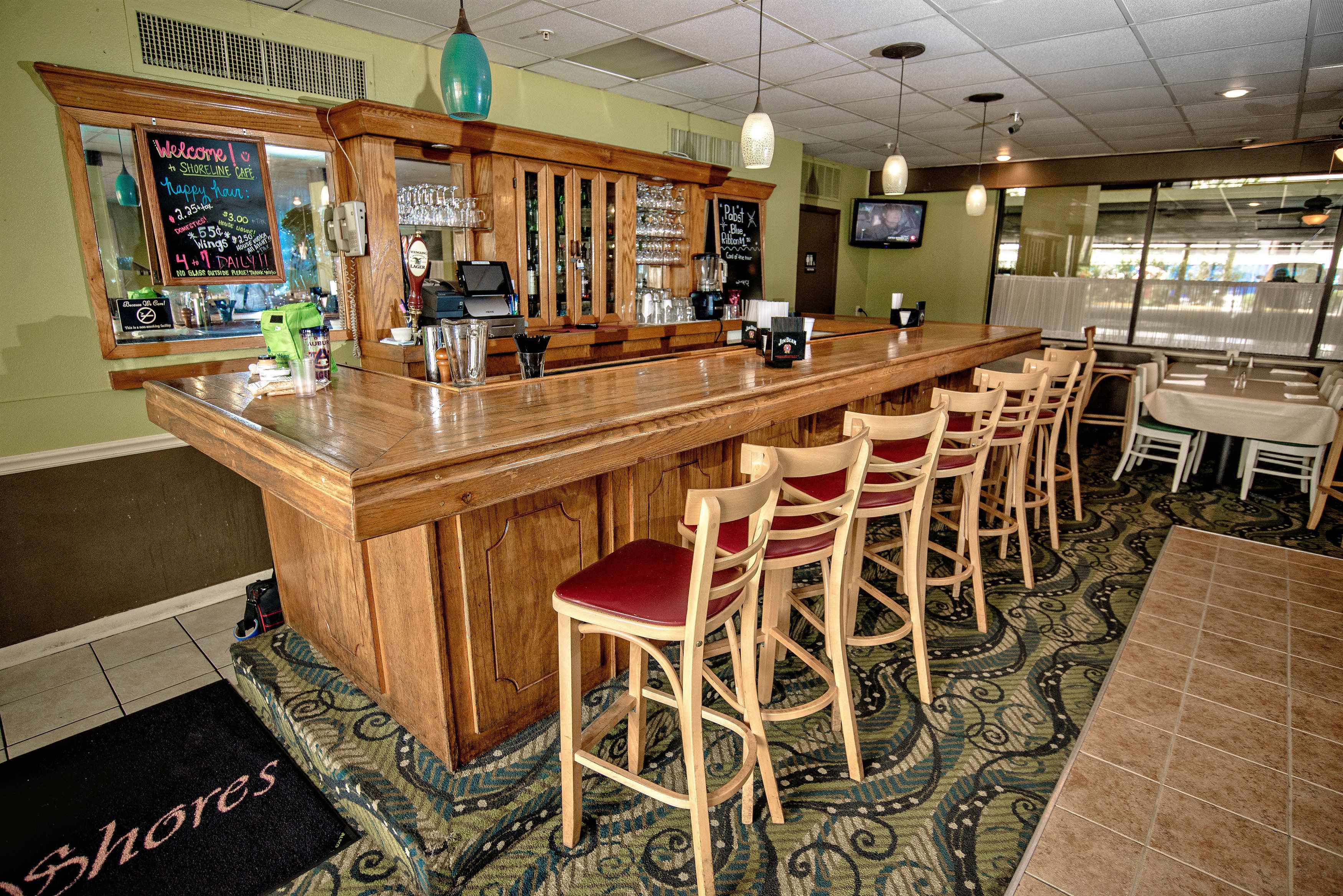 Een bar met een houten toonbank, barstoelen en een krijtbordmenu.