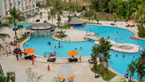Una gran piscina al aire libre con múltiples carriles, rodeada de palmeras y zonas de descanso.
