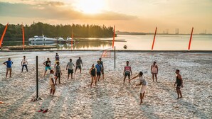 Partido de voleibol de playa con un atardecer de fondo.