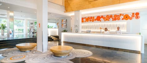A modern hotel lobby with a reception desk, wooden accents, and a view of the outdoors.