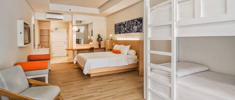 A modern hotel room with a bed, a seating area with chairs, a desk, and a bunk bed.