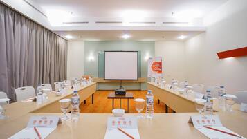 A conference room with a long table, chairs, water bottles, glasses, and a projector screen.
