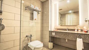 A modern bathroom with a glass shower enclosure, a toilet with a towel on the seat, a sink with a towel rack, and a mirror above the sink.