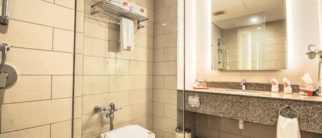 A modern bathroom with a glass shower enclosure, a toilet with a towel on the seat, a sink with a towel rack, and a mirror above the sink.
