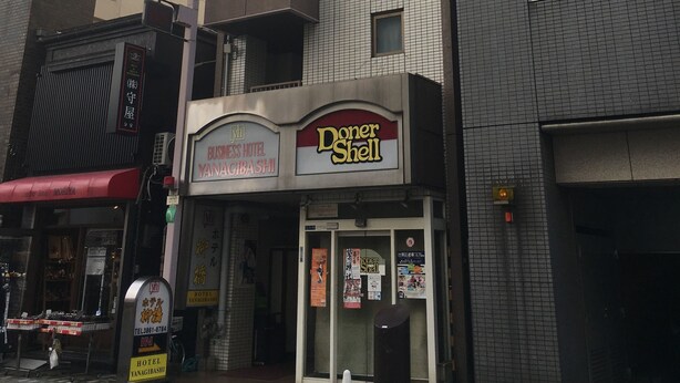 Un hotel con un letrero de 'Doner Shell', un letrero de 'BUSINESS HOTEL YANAGIBASHI' y un letrero de 'HOTEL YANAGIBASHI'.