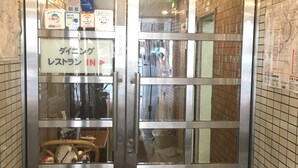 Entrada de un hotel con un letrero en japonés, un símbolo de Wi-Fi y una señalización que indica el restaurante y los baños.