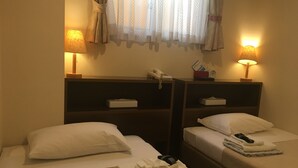 Habitación de hotel con dos camas, cada una con una almohada y una toalla doblada. Hay mesitas de noche con lámparas y un teléfono.