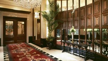 A grand lobby with a red carpet, a large chandelier, and a wooden panel wall with windows.