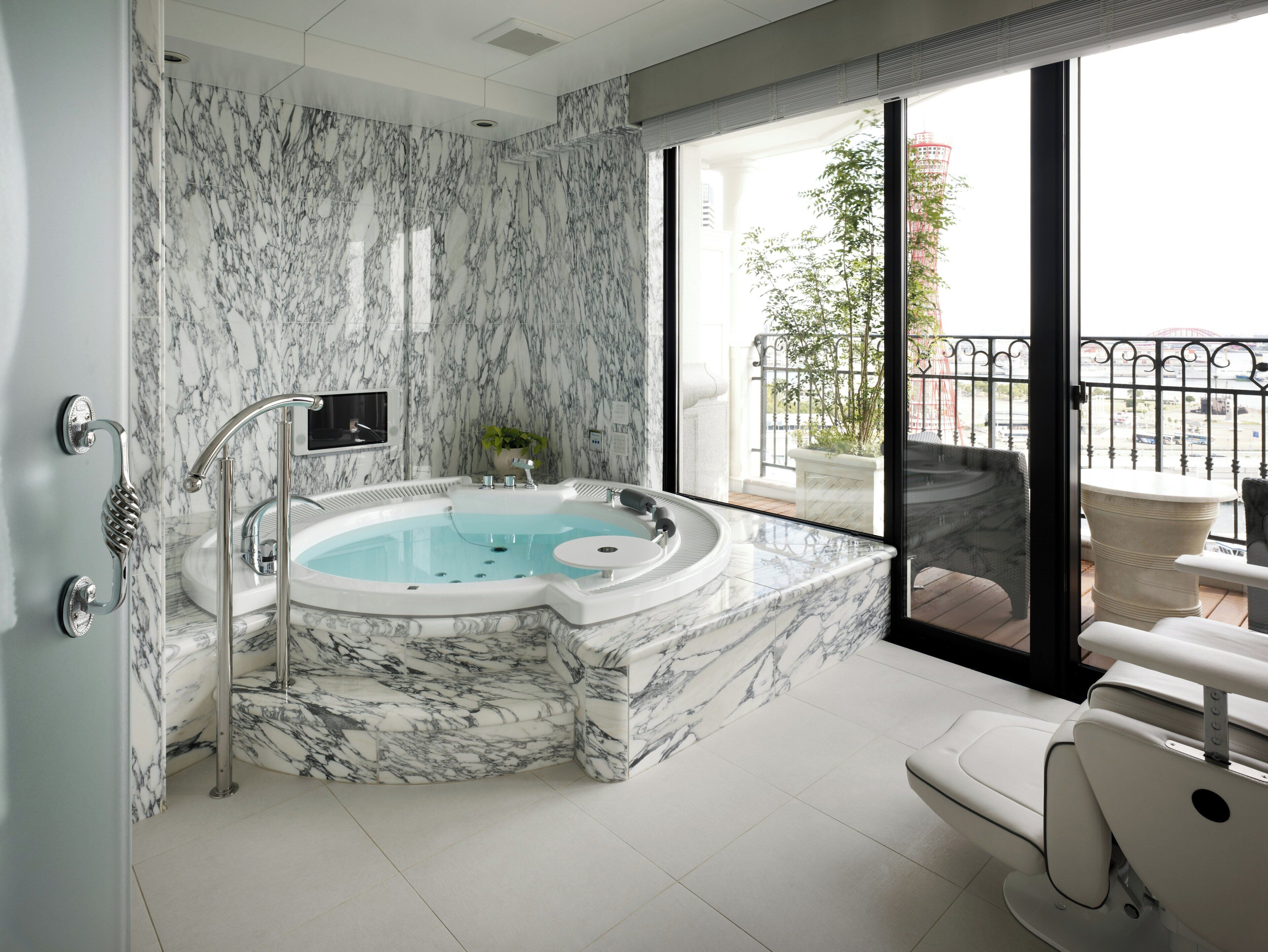 A bathroom with a marble wall, a hot tub, a sink, a toilet, and a view of a balcony with a railing.