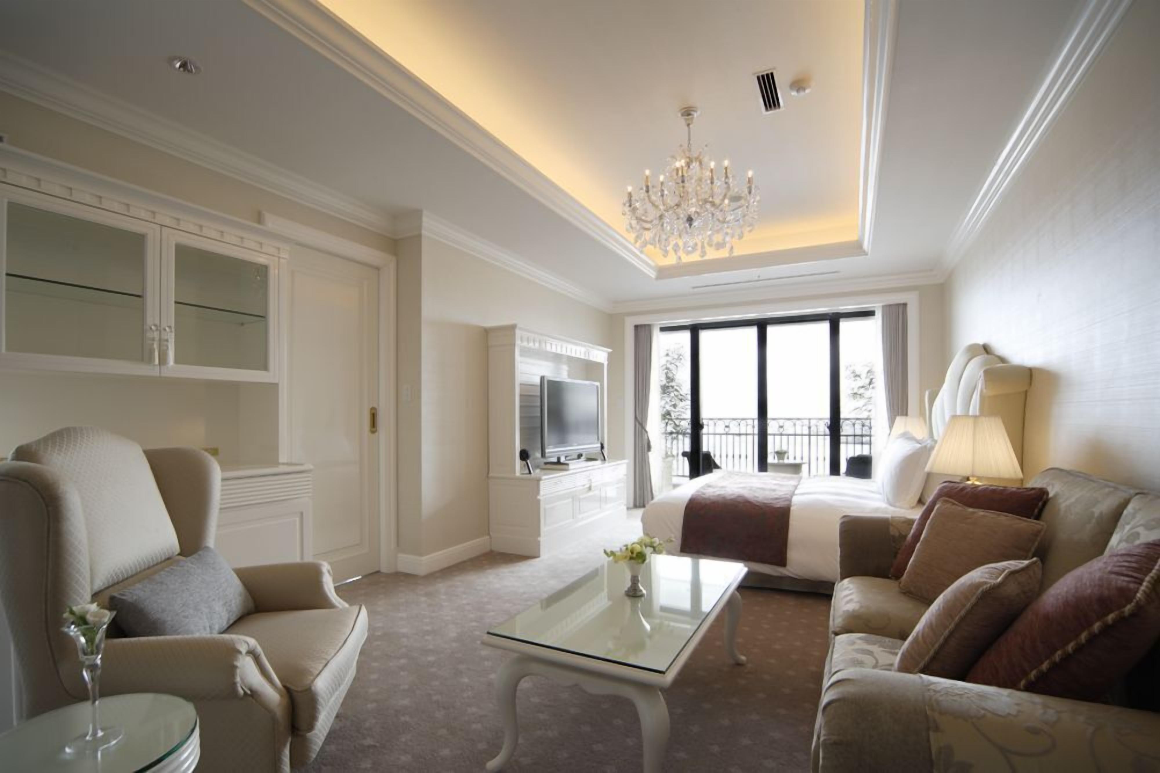 Un amplio salón con candelabro, televisor y vistas al balcón.