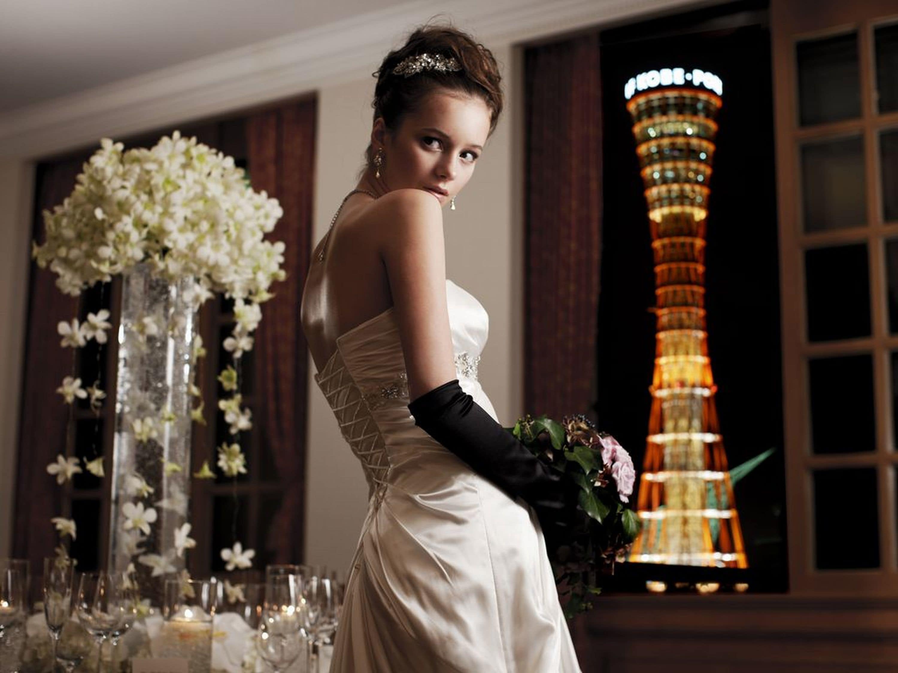 A wedding venue with a large floral arrangement, a tall illuminated tower in the background, and a table set with glasses and candles.