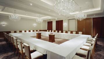 A large conference room with a long table, multiple chairs, and chandeliers.