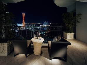 A rooftop terrace with wicker furniture, a table with a bottle and glasses, and a cityscape view at night. - Hotel La Suite Kobe Harborland (Kobe)