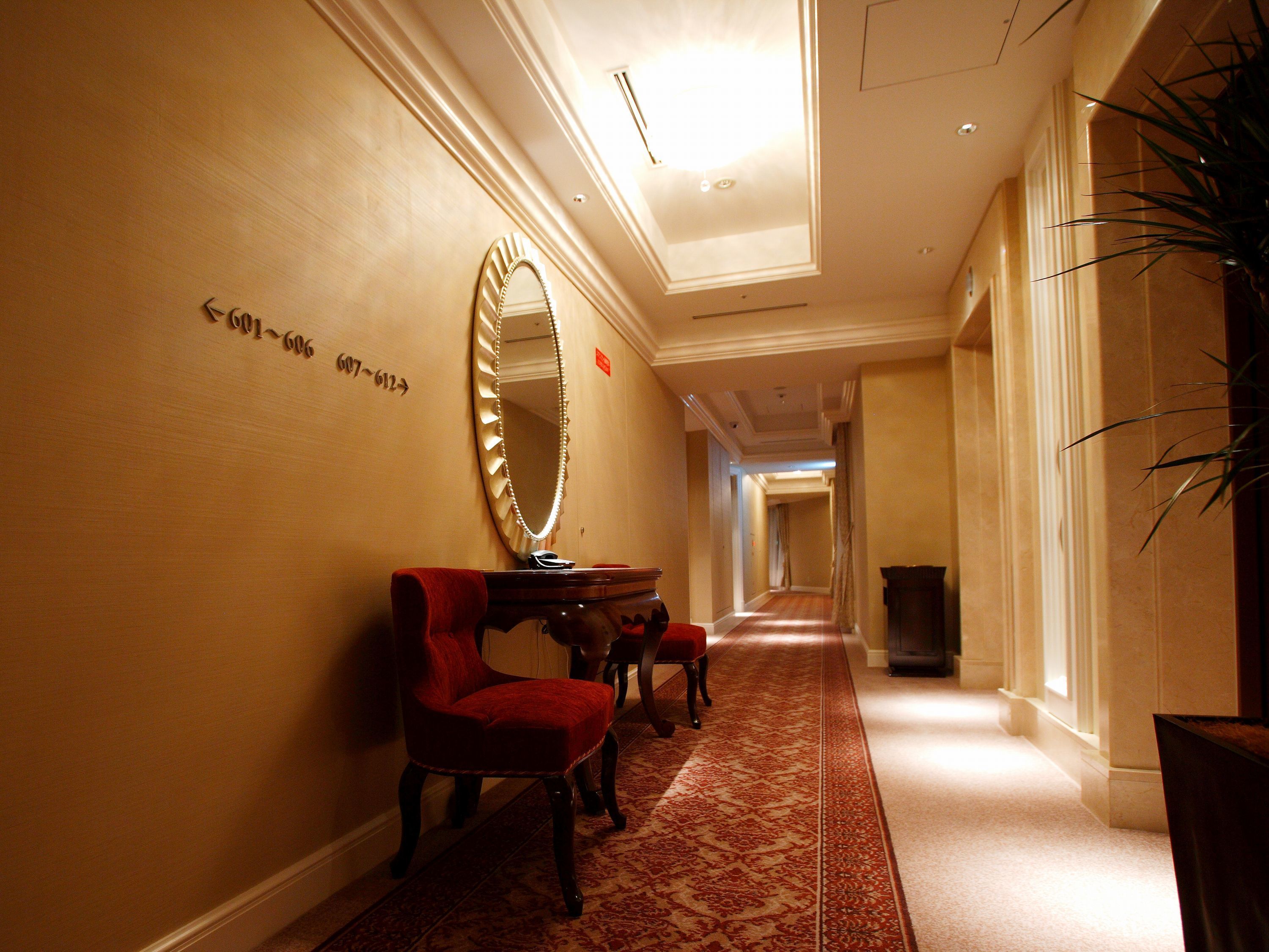 A hotel hallway with a red chair, a large mirror, and a red carpet.
