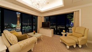 A modern living room with a large TV, comfortable seating, a chandelier, and a view of a cityscape at night. - Hotel La Suite Kobe Harborland (Kobe)
