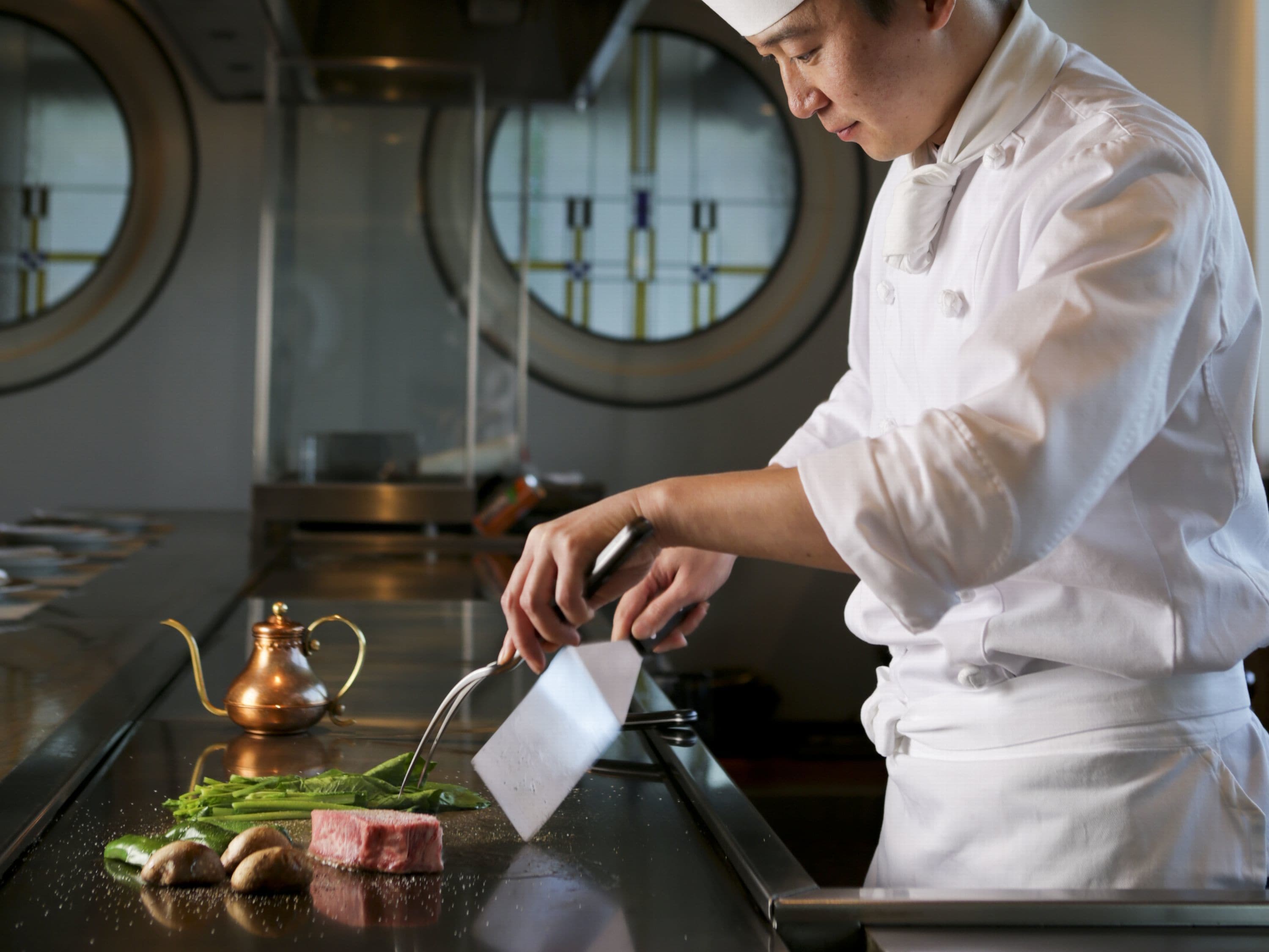 A chef in a white uniform preparing food on a hot plate in a kitchen.
