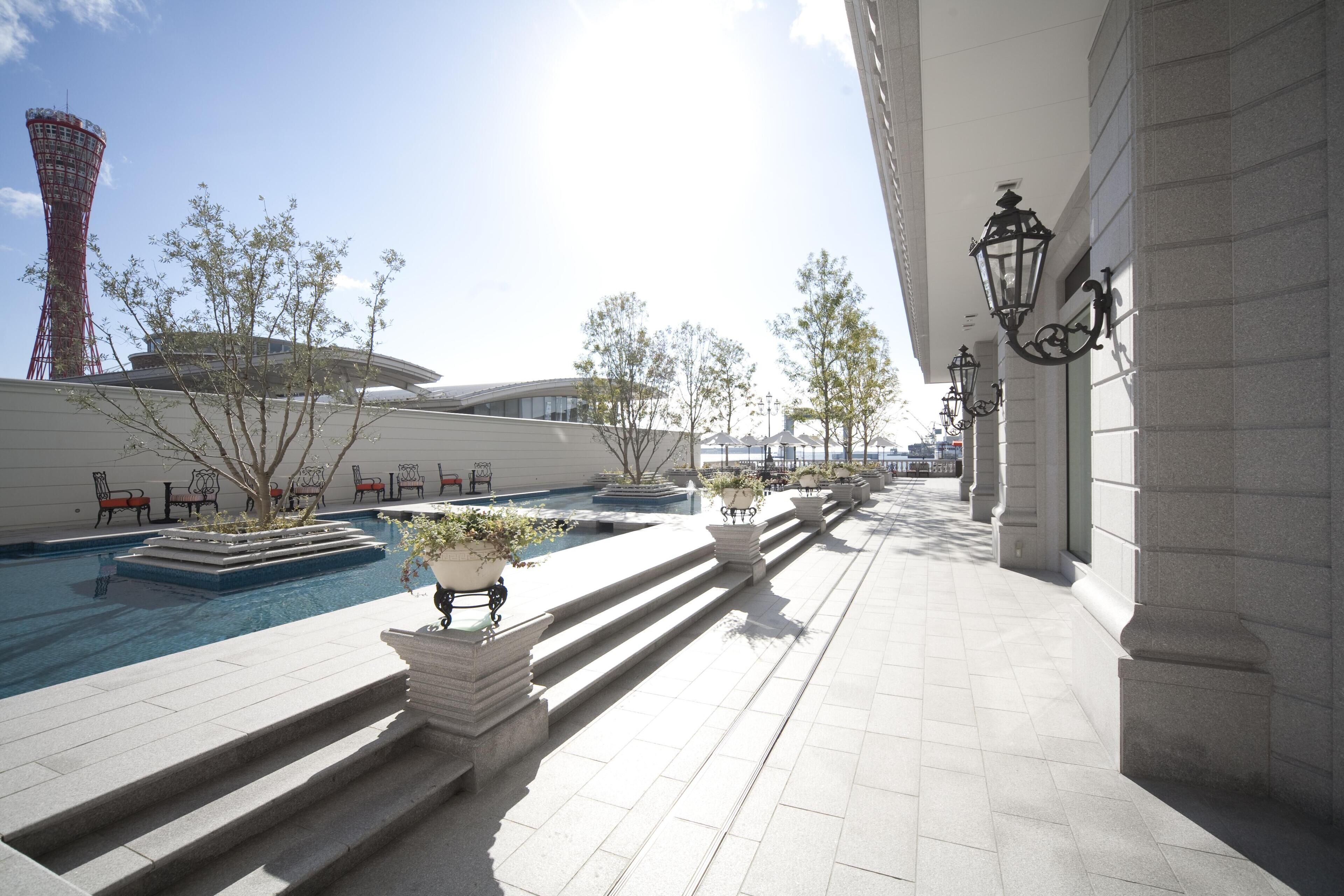 A rooftop pool area with steps leading down to a pool, surrounded by potted plants and outdoor furniture.