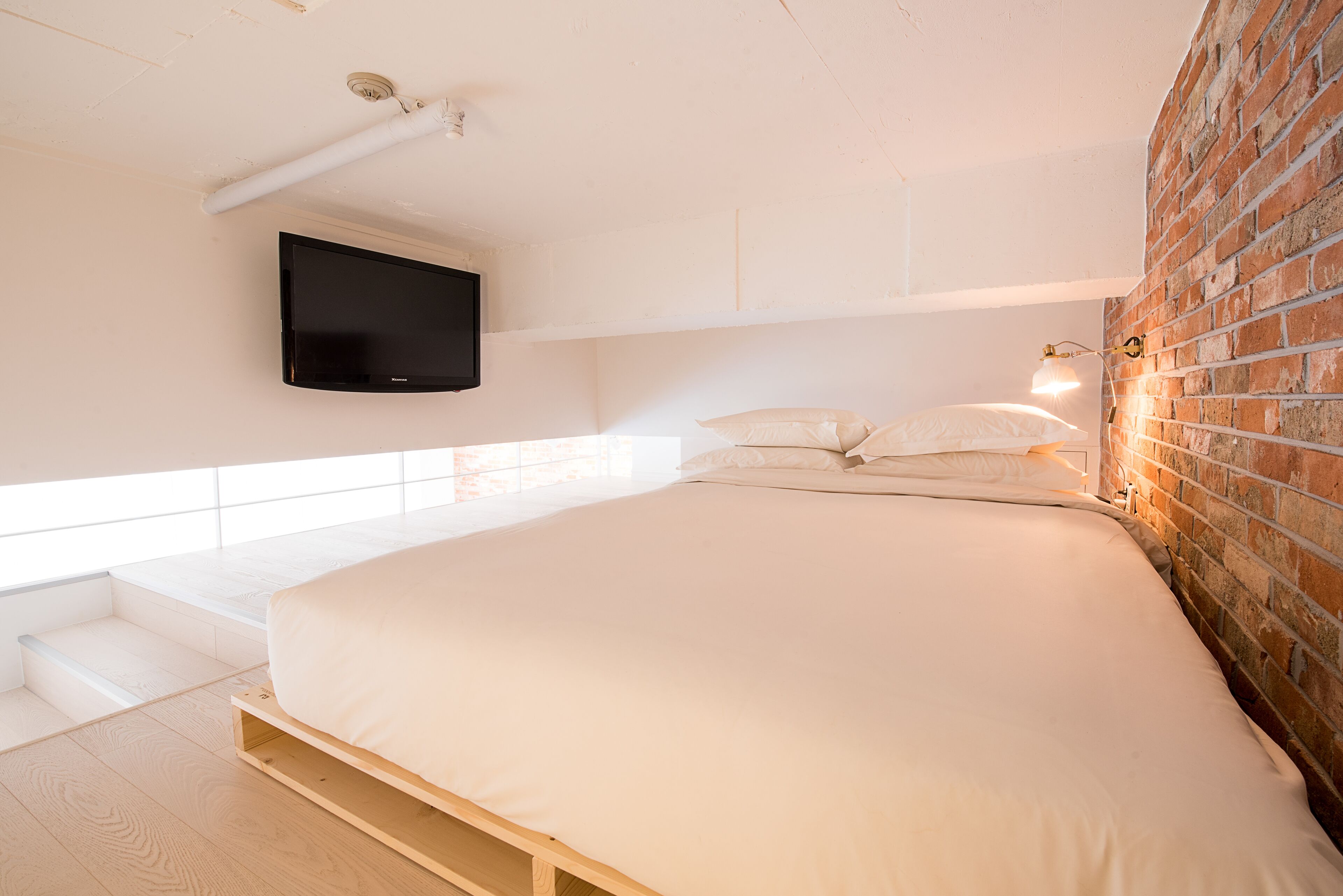 Un dormitorio con una cama grande, un televisor montado y una pared de ladrillo.
