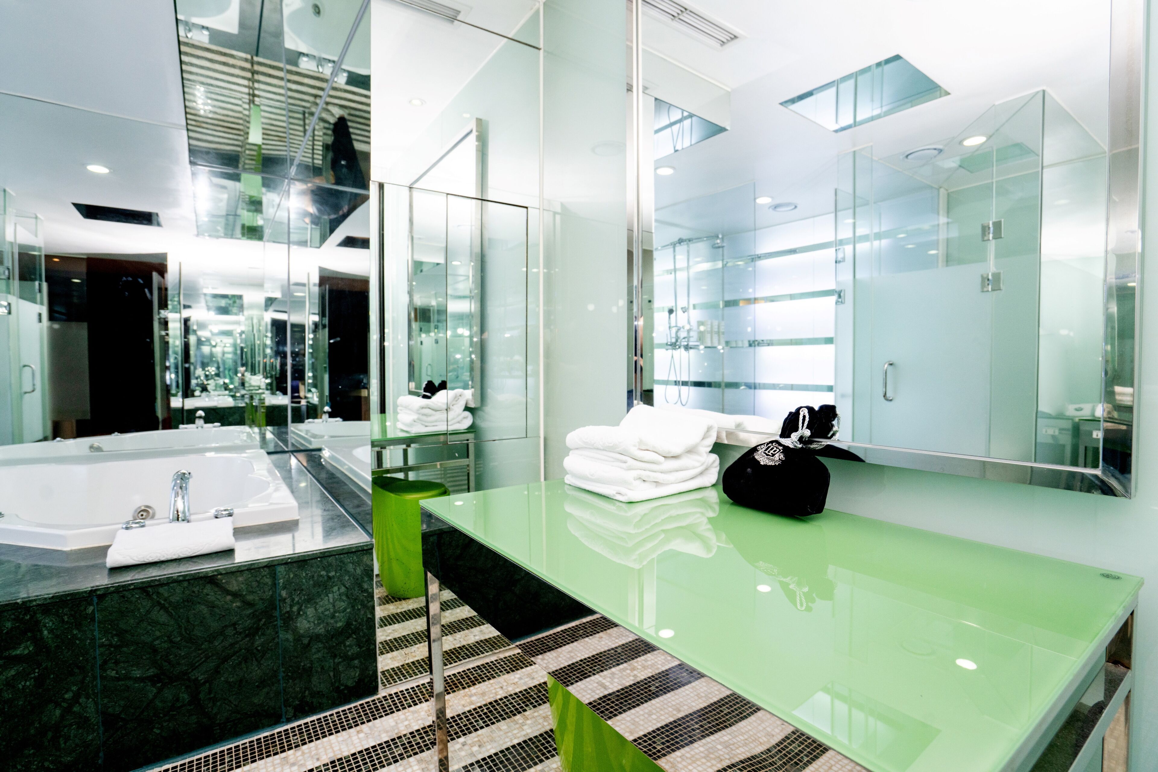 Un baño moderno con cabina de ducha de vidrio, tocador verde y un espejo grande.