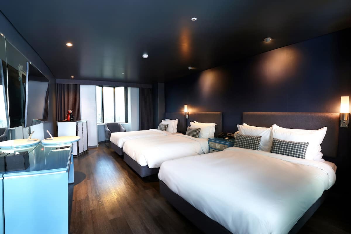 Une chambre d’hôtel avec deux lits, un bureau, une chaise et une grande fenêtre.