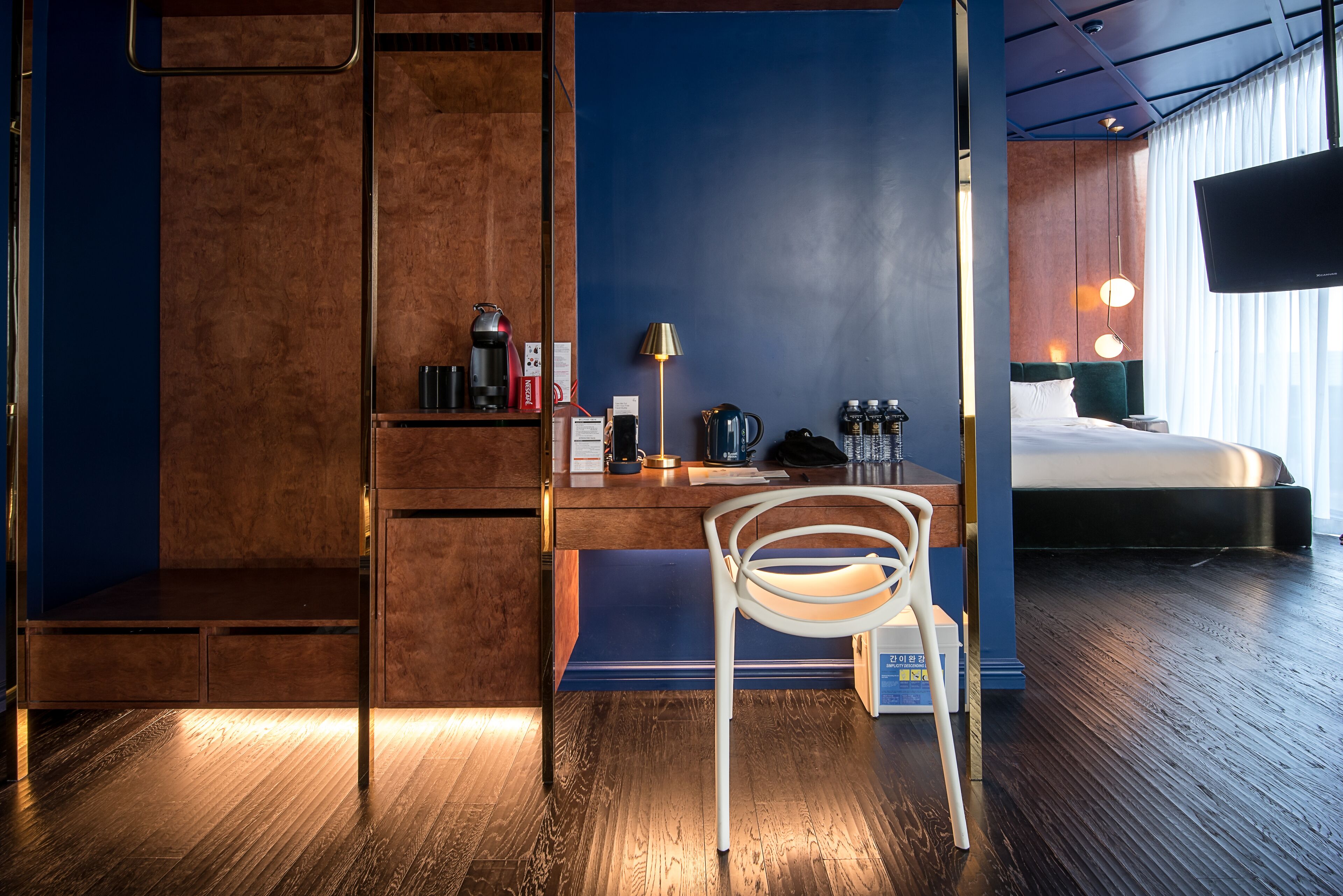 Ein modernes Hotelzimmer mit einem Holztisch, einem Stuhl, einem Bett, einem Fernseher und einem Nachttisch mit Lampe.