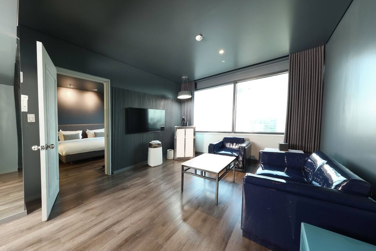 Un salon moderne avec un canapé, une table basse, un téléviseur et un lit à l’arrière-plan.