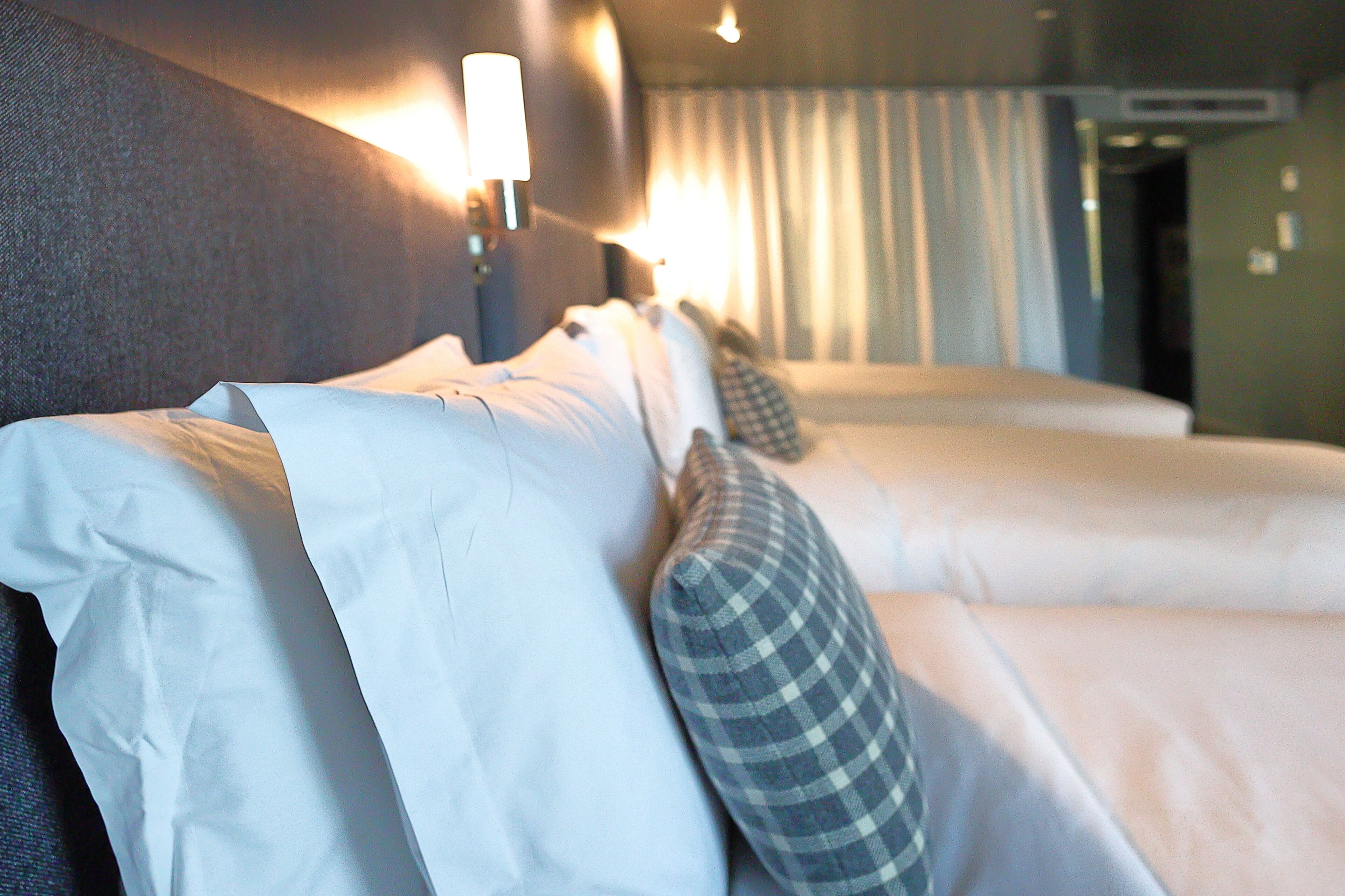 A hotel room with two beds, a headboard, and a wall-mounted lamp.