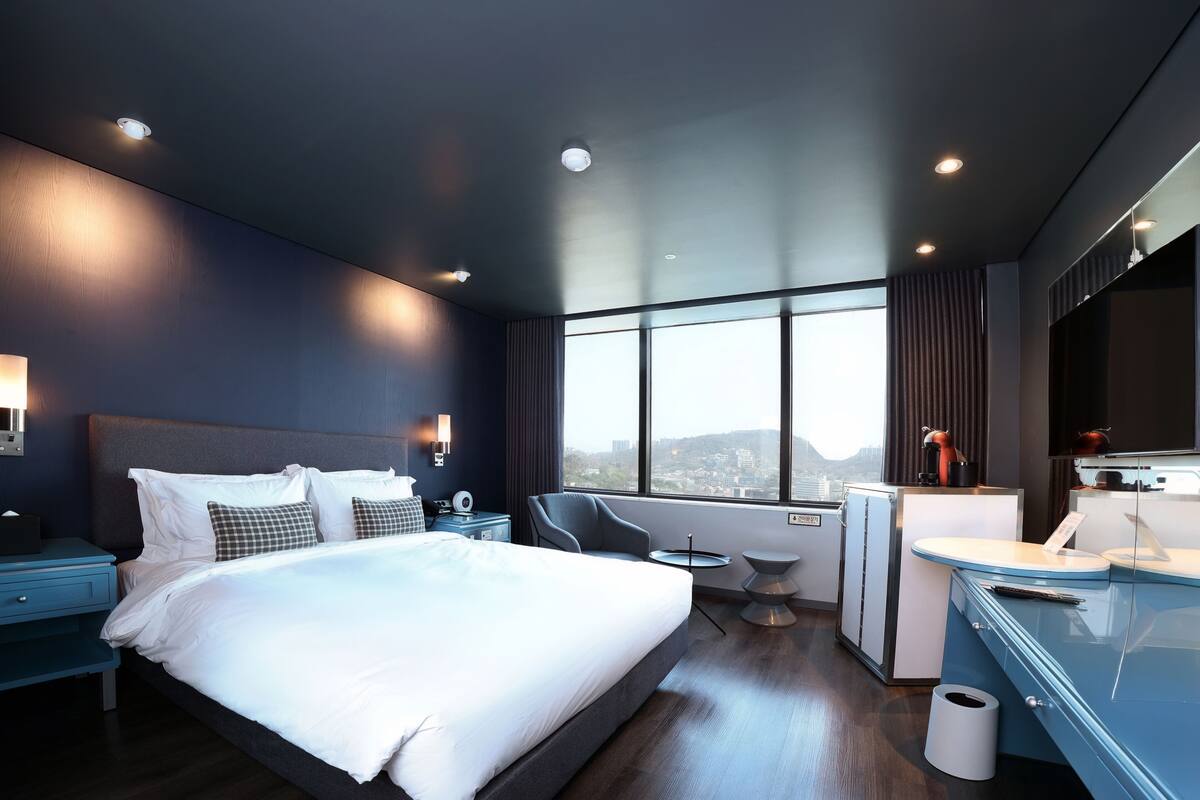 Une chambre d’hôtel moderne avec un grand lit, un bureau, une chaise et une vue sur la ville.