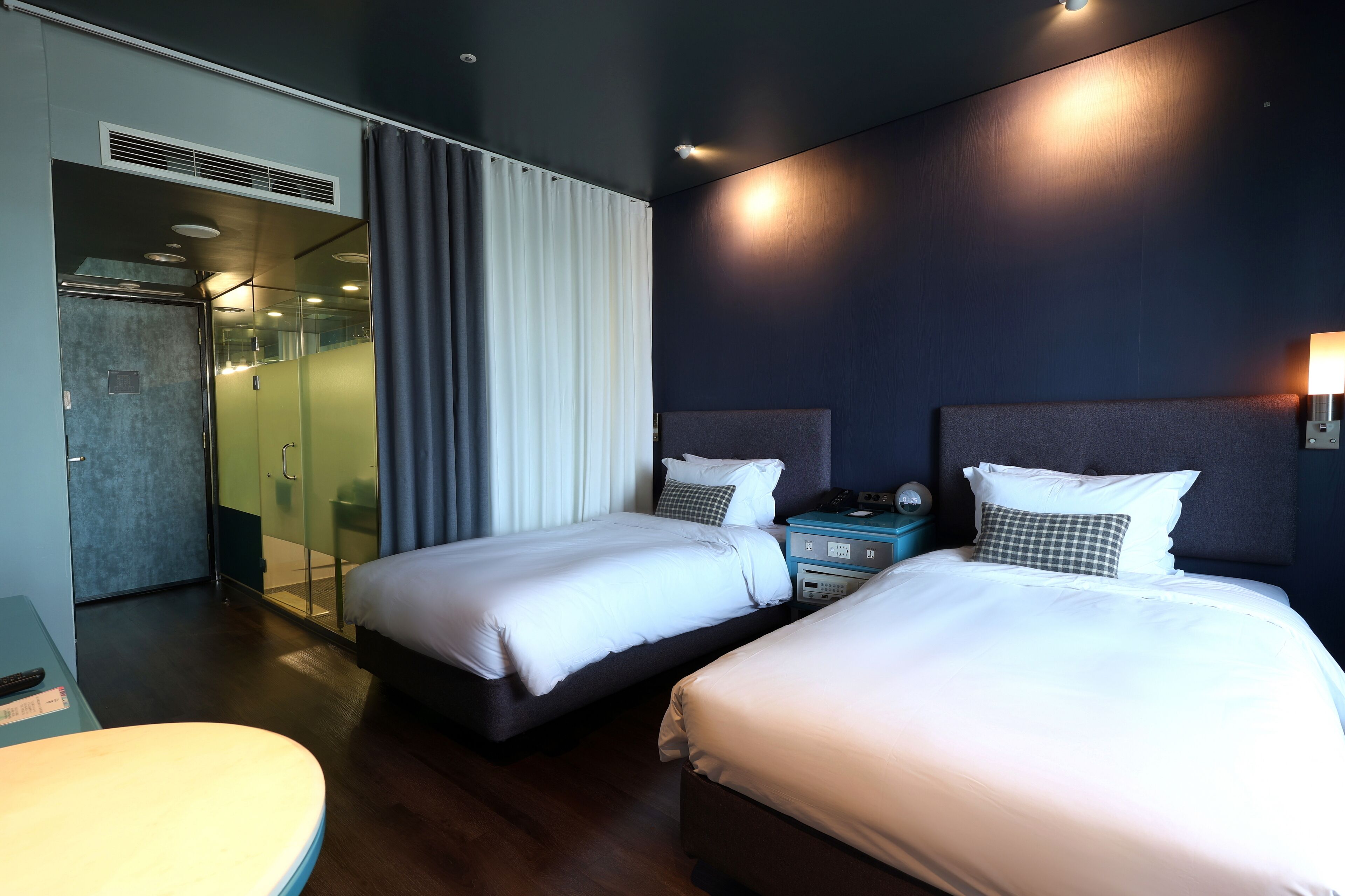 Hotelkamer met twee bedden, een glazen douchecabine, een nachtkastje met lamp en een telefoon aan de muur.