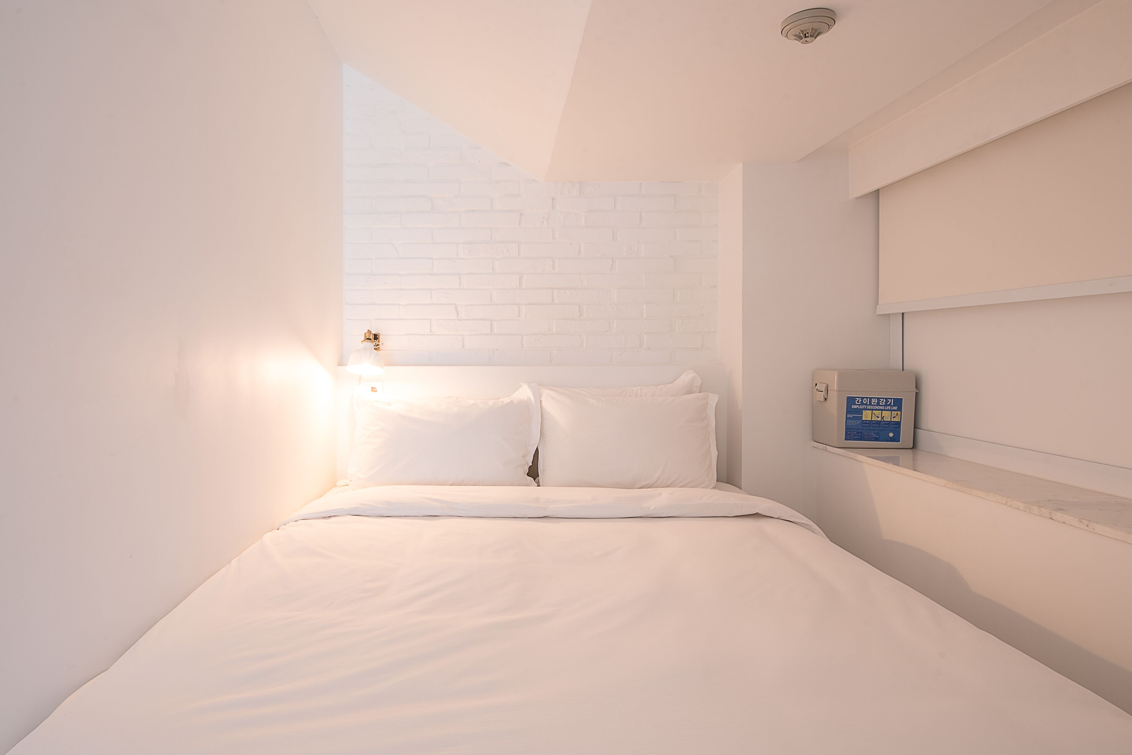 Ein modernes Schlafzimmer mit weißer Backsteinwand, einem Bett mit weißer Bettwäsche und einer Bedienkonsole an der Wand.