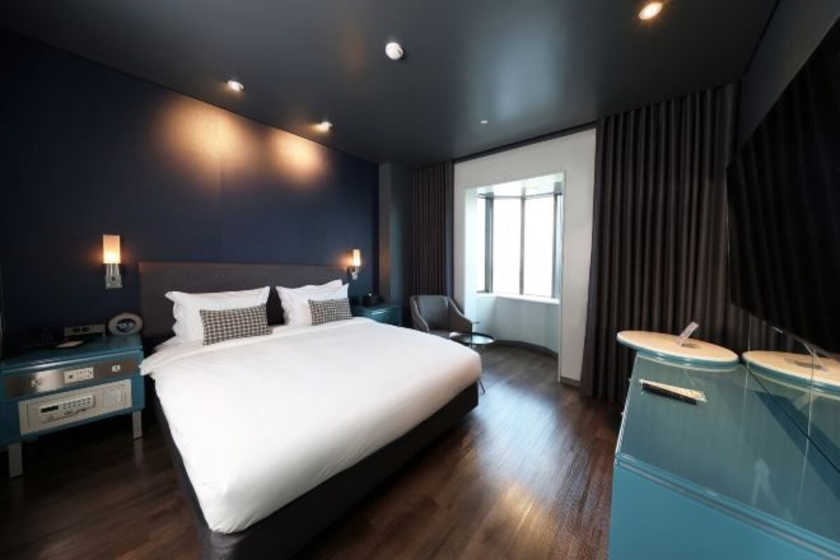 Quarto de hotel moderno com uma cama grande, mesas de cabeceira, uma escrivaninha e um guarda-roupa.
